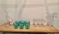 Overview of green margarita glasses, clear wine glasses, pitcher, and decanter on wooden surface