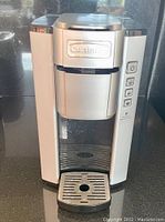 Front view of the silver and black Cuisinart coffee brewer showing power and function buttons on the right side and drip tray below dispenser.