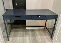 Front angled view showing the desk with two drawers and metal frame on a wood floor.