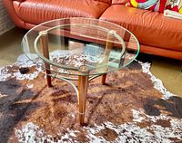 Front angle showing circular glass top, wooden legs with metal rings, and metal support brace.