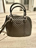 Front view of the black purse showing embossed G pattern and two handles.