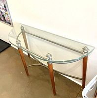Front angled view showing the glass table top, wooden legs, and metal support bars.