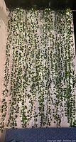 Front view of curtain with hanging green leaves and integrated LED lights on a white background, showing full coverage and light strands.