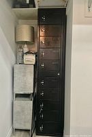 Photo of locked tall black metal locker with multiple compartments next to a lamp and other furniture.