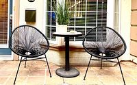 Two black string lounge chairs flanking a round patio table on tiled floor
