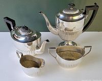 Four piece coffee and tea service set arranged together showing polished silver plated items with ribbed lower sections and black handles.