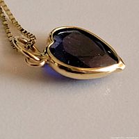 Close-up of heart-shaped sapphire pendant in gold bezel on chain.