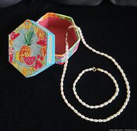 Freshwater pearl necklace and bracelet displayed with the hexagonal fruit-themed paperboard box on black background.