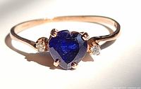 Front-on close-up of heart-shaped sapphire and flanking diamonds set in rose gold band
