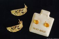 Two pairs of earrings shown on black background, one pair gold floral design and one pair yellow sapphire studs in original white holder marked 10kt gold.