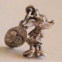 Close-up side view of vintage sterling silver Minnie Mouse pendant with attached tag showing Mickey Mouse head silhouette pattern.