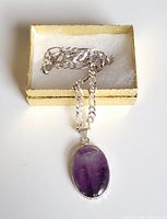 Sterling silver necklace with chunky chain and large oval amethyst pendant displayed in gold gift box with white padding on the inside.