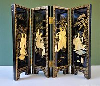 Front view of the four-panel black lacquered wood folding screen with gold painted designs and raised mother of pearl geisha figures.