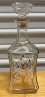 Front view of one vintage glass liquor decanter showing hand-painted white and gold pear tree and bird detail on thick walled glass with faceted stopper.