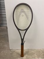Full view of the grey graphite tennis racquet with brown leather grip and stringing visible, showing overall condition and shape.