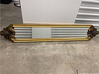 Full view of the elongated rectangular carved wood Bombay Co. Montague mirror lying horizontally on the floor.