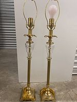 Front view of the two complete lamps showing brass bases, cut crystal centers, and original harps and finials, one lamp with an exposed bulb.