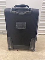 Front view of black Brookstone carry on suitcase showing handle, wheels, and front seam damage.