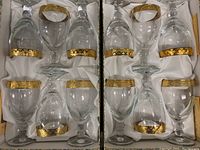 Two open gift boxes containing 12 gold-rimmed lead crystal wine glasses with square geometric patterns.