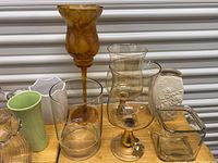 Multiple vases and candle holders of various shapes including amber glass, clear glass, green ceramic, and white embossed ceramic.