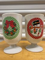 Two white pedestal mugs with Christmas wreath and snowman decorations on polka dot backgrounds