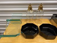 Photo showing clear glass CD holder with green edges, two black octagonal trays or napkin rings, and two glass soap or lotion dispensers with gold pump tops
