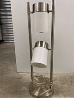 Front view of the modern brushed steel floor lamp showing two bulbs with frosted glass shades aligned vertically on frame.