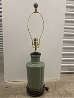 Full view of the sea foam green ceramic lamp with black harp and round finial. Lamp cord coiled at bottom.