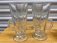 Four clear glass pedestal mugs with handles, each printed with 'E&J Cask & Cream Liqueur' logo.