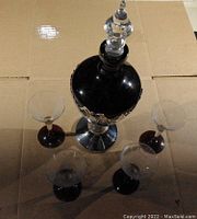 Top view of decanter surrounded by 4 glasses showing clear glass bowls with purple bases and decorative silver overlay on decanter