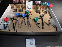 Overview of multiple darts with different flights arranged in a box along with packages of spare tips and feathers