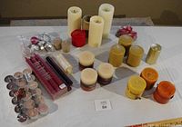 Photo showing multiple candles arranged on a table including pillar candles in cream, yellow, and orange colors, taper candles in burgundy and cream, numerous silver foil tea light candles, and a small red pillar candle.