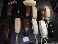 Top view of first set of 13 Trimline telephones all laid out on black surface, showing handset colors and cord types.
