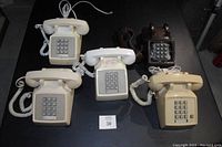 Five vintage push button desk phones in beige, cream, white, and brown colors arranged on a table.