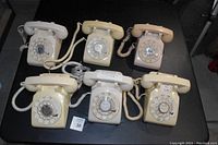 Top view of six vintage Bell/Western Electric rotary dial desk phones arranged in two rows on a black surface