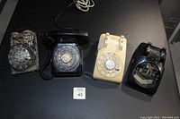Four vintage rotary phones displayed on a dark surface, showing condition and included items.