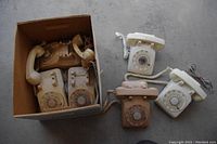 Full view of six vintage rotary dial telephones, some outside and some inside a cardboard box.