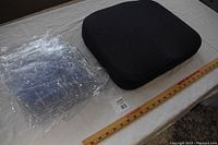Shows the Tempurpedic chair pad next to the plastic chair covers on a table with a ruler for scale.