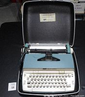 Front view of Smith Corona electric typewriter inside hard carrying case, keyboard and paper feeding mechanism visible.