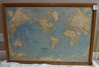 Photo of the vintage National Geographic world map framed in wood, showing the full map and frame with some visible wear.