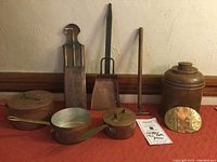 Full view of lot on red cloth showing all copper items: pots, tins, belt buckle, and tools.