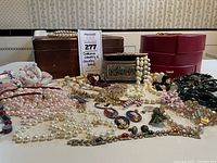 Photo showing full assortment of costume jewelry and three jewelry boxes including pearl-like beads, cloisonné pendants, and decorative boxes in red, wood, and metal.
