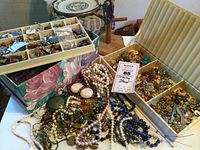 Overall view of two compartment trays filled with jewelry and loose necklaces on table