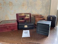 Photo showing six jewelry storage boxes of various styles and materials on a wooden surface with floral wallpaper background