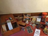Overall view of lot on red tablecloth showing wooden box, glassware, tins, boxes and small items