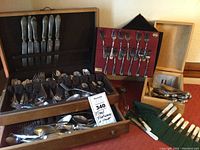 Overview of flatware chest open with assorted pieces, red carrier, green roll and small wooden box