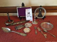 Wide view of the full lot on red cloth showing candlesticks, frames, flatware, glass dish, coin purse and small cases