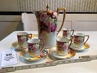 Photo showing the full Nippon chocolate set with floral design including the pot, five cups, and six saucers arranged with a ruler for scale.