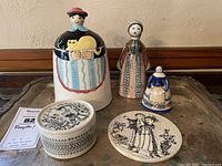 All lot items arranged together showing cookie jar, two pottery ladies, and Bjorn Winblad dish and plaque.