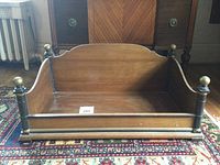 Full view of rectangular wooden pet bed on decorative rug, showing wood finish and finials